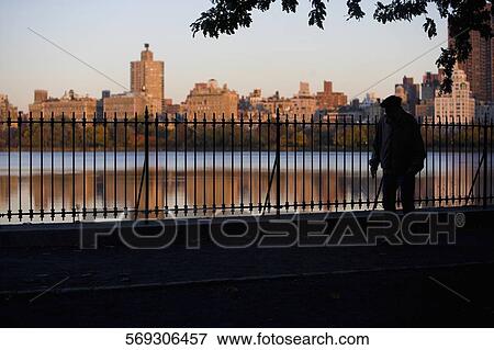 Silhouette of a man walking near a railing with buildings in the background, Central Park, Manhattan, New York City, New York State, USA View Large Photo Image Stock Photo - Silhouette of a man walking near a railing with buildings in the background, Central Park, Manhattan, New York City, New York State, USA. Fotosearch
