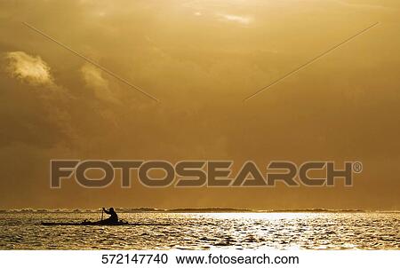 Stock Image - Silhouette of a person rowing a boat, Tahiti, French Polynesia. Fotosearch