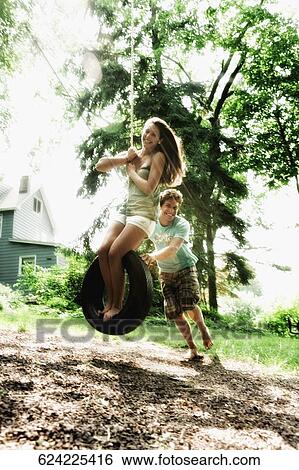 Teenage girl swinging on a tire swing with a young man pushing her View Large Photo Image Stock Photograph - Teenage girl swinging on a tire swing with a young man pushing her. Fotosearch