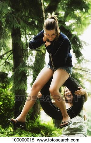 Teenage girl swinging on a tire swing with her friend pulling her View Large Photo Image Stock Photography - Teenage girl swinging on a tire swing with her friend pulling her. Fotosearch