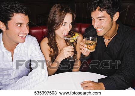Stock Image - Three friends sitting on a booth and smiling. Fotosearch