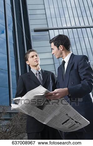 Two businessmen looking at each other and holding a newspaper View Large Photo Image Stock Photo - Two businessmen looking at each other and holding a newspaper. Fotosearch