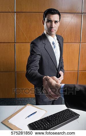 Stock Image - Two businessmen shaking her hands. Fotosearch