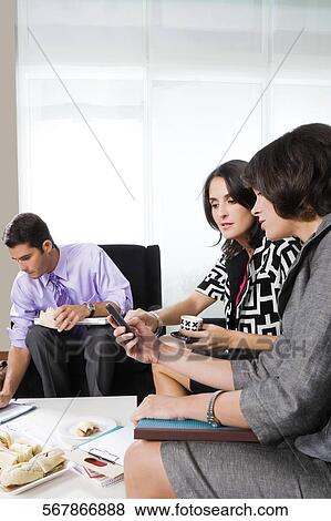 Stock Photo - Two businesswomen looking at a mobile phone. Fotosearch