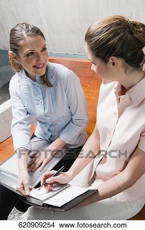 Two businesswomen sitting on a bench and smiling View Large Photo Image Picture - Two businesswomen sitting on a bench and smiling. Fotosearch