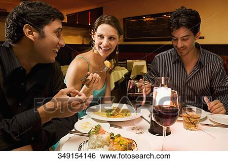 Two young men with a young woman eating food in a restaurant View Large Photo Image Stock Photograph - Two young men with a young woman eating food in a restaurant. Fotosearch