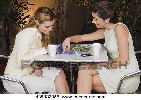 Two young women sitting in a cafe and smiling View Large Photo Image Stock Photo - Two young women sitting in a cafe and smiling. Fotosearch