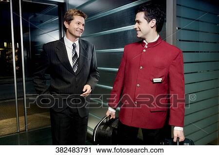 Waiter holding luggage and a businessman standing behind him View Large Photo Image Stock Image - Waiter holding luggage and a businessman standing behind him. Fotosearch