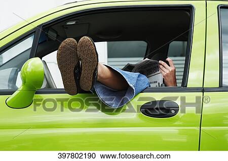 Woman holding a newspaper with her legs resting on a car window View Large Photo Image Stock Image - Woman holding a newspaper with her legs resting on a car window. Fotosearch