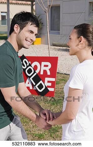Young couple holding hands of each other in front of a sold information board View Large Photo Image Stock Image - Young couple holding hands of each other in front of a sold information board. Fotosearch