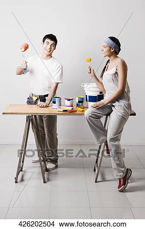 Picture - Young couple holding paint rollers and smiling. Fotosearch