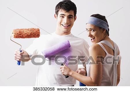 Young couple holding paint rollers and smiling View Large Photo Image Stock Photo - Young couple holding paint rollers and smiling. Fotosearch