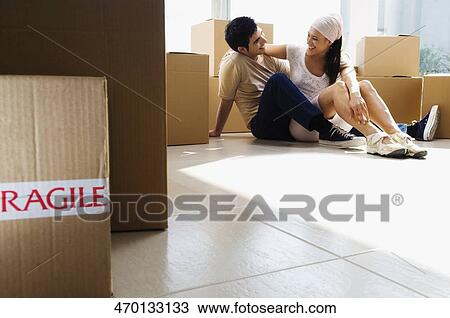 Stock Image - Young couple sitting on the floor and smiling. Fotosearch