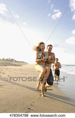 Stock Photo - Young man carrying a young woman on the beach. Fotosearch