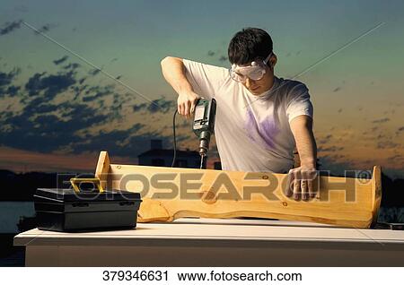 Young man drilling a wooden plank View Large Photo Image Stock Image - Young man drilling a wooden plank. Fotosearch