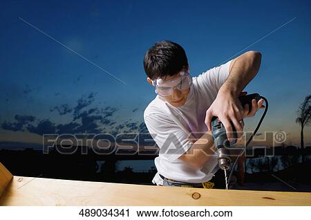 Young man drilling a wooden plank View Large Photo Image Stock Image - Young man drilling a wooden plank. Fotosearch
