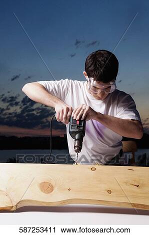 Young man drilling a wooden plank View Large Photo Image Stock Image - Young man drilling a wooden plank. Fotosearch