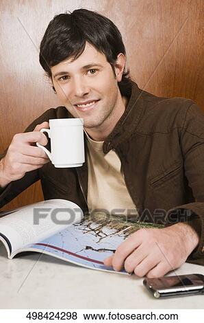Young man drinking coffee in a cafe and smiling View Large Photo Image Stock Photo - Young man drinking coffee in a cafe and smiling. Fotosearch