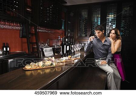 Young man drinking wine at a bar counter with a mid adult woman standing beside him View Large Photo Image Stock Photo - Young man drinking wine at a bar counter with a mid adult woman standing beside him. Fotosearch