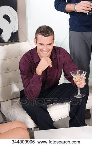 Stock Photograph - Young man holding a glass of martini and smiling. Fotosearch