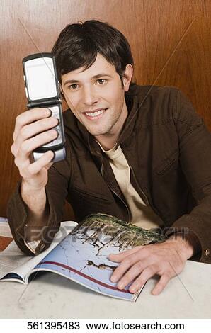 Young man holding a mobile phone in a cafe and smiling View Large Photo Image Stock Image - Young man holding a mobile phone in a cafe and smiling. Fotosearch
