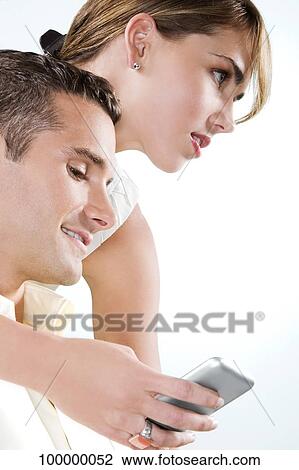 Young man looking at a mobile phone with a young woman beside him View Large Photo Image Stock Image - Young man looking at a mobile phone with a young woman beside him. Fotosearch