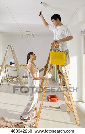 Young man painting the wall and a young woman holding a step ladder View Large Photo Image Stock Photo - Young man painting the wall and a young woman holding a step ladder. Fotosearch