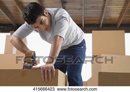 Young man pasting adhesive tape on a cardboard box View Large Photo Image Stock Image - Young man pasting adhesive tape on a cardboard box. Fotosearch