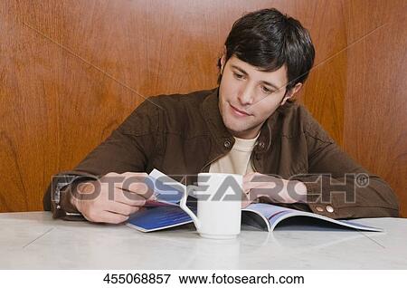Young man reading a magazine in a cafe View Large Photo Image Stock Photo - Young man reading a magazine in a cafe. Fotosearch