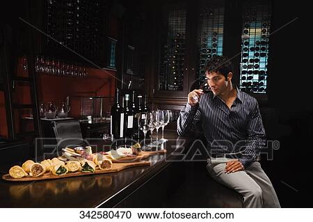 Stock Image - Young man sitting at a bar counter and drinking wine. Fotosearch