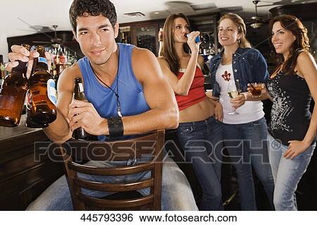 Young man sitting at a bar counter with his three friends standing behind him View Large Photo Image Stock Photograph - Young man sitting at a bar counter with his three friends standing behind him. Fotosearch