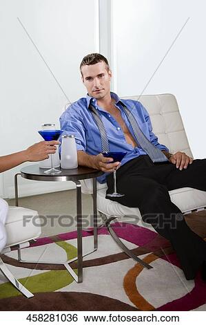 Stock Photograph - Young man sitting on a chair and holding a glass of cocktail. Fotosearch