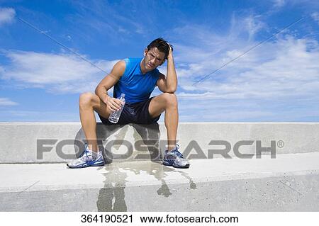 Young man sitting on a ledge and holding a water bottle View Large Photo Image Stock Image - Young man sitting on a ledge and holding a water bottle. Fotosearch