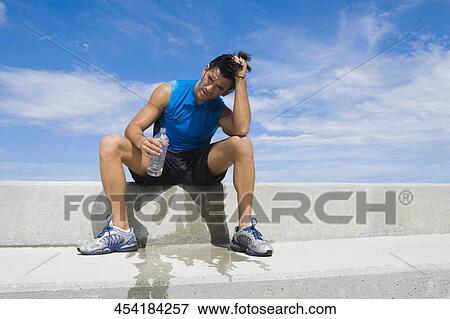 Young man sitting on the ledge and holding a water bottle View Large Photo Image Stock Photo - Young man sitting on the ledge and holding a water bottle. Fotosearch