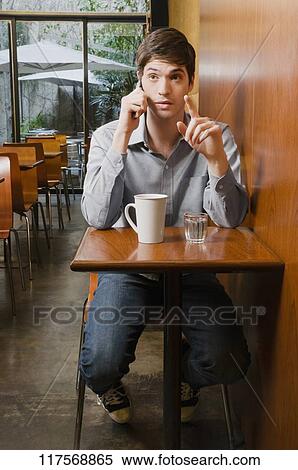 Young man talking on a mobile phone in a cafe View Large Photo Image Stock Photography - Young man talking on a mobile phone in a cafe. Fotosearch