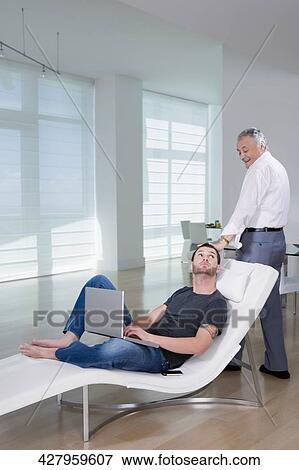 Young man using a laptop with his grandfather standing behind him View Large Photo Image Stock Photo - Young man using a laptop with his grandfather standing behind him. Fotosearch
