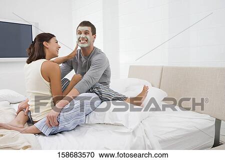 Stock Image - Young woman applying facial mask on a young man's face. Fotosearch