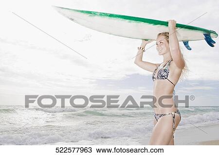 Young woman carrying a surfboard on the beach View Large Photo Image Stock Image - Young woman carrying a surfboard on the beach. Fotosearch