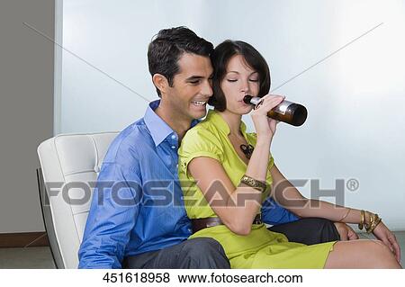 Young woman drinking beer and sitting with a mid adult man on a chair View Large Photo Image Stock Photo - Young woman drinking beer and sitting with a mid adult man on a chair. Fotosearch