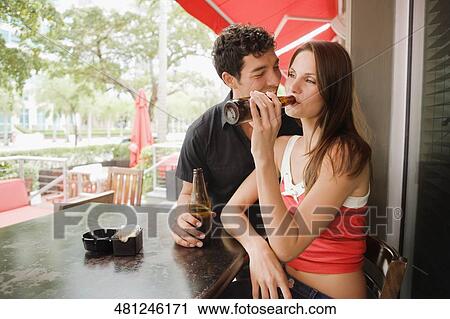 Young woman drinking beer with a young man sitting beside her and smiling View Large Photo Image Stock Image - Young woman drinking beer with a young man sitting beside her and smiling. Fotosearch