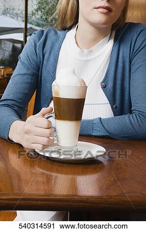 Young woman holding a glass of cappuccino View Large Photo Image Stock Image - Young woman holding a glass of cappuccino. Fotosearch