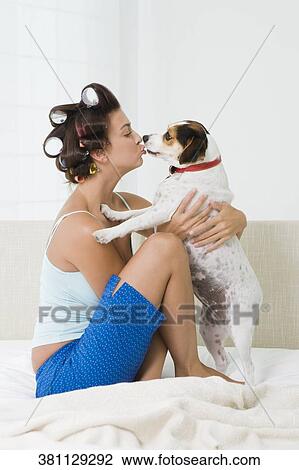 Stock Image - Young woman kissing a puppy on the bed. Fotosearch