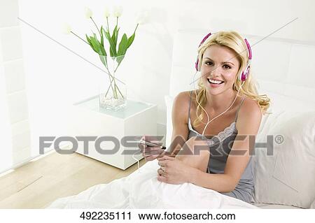 Young woman listening to an MP3 player and smiling View Large Photo Image Stock Image - Young woman listening to an MP3 player and smiling. Fotosearch
