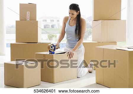 Stock Image - Young woman pasting adhesive tape on a cardboard box. Fotosearch