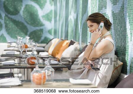 Young woman sitting in a restaurant and talking on a mobile phone View Large Photo Image Stock Photo - Young woman sitting in a restaurant and talking on a mobile phone. Fotosearch