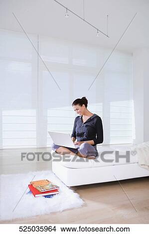 Young woman sitting on the bed and using a laptop View Large Photo Image Picture - Young woman sitting on the bed and using a laptop. Fotosearch