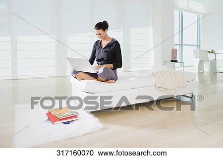 Young woman sitting on the bed and using a laptop View Large Photo Image Stock Image - Young woman sitting on the bed and using a laptop. Fotosearch