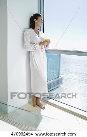 Picture - Young woman standing and holding a glass of juice. Fotosearch