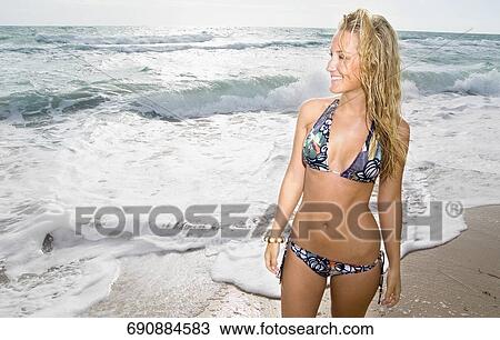 Stock Image - Young woman standing on the beach and smiling. Fotosearch