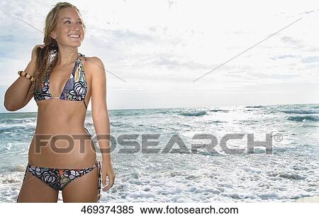 Stock Photography - Young woman standing on the beach and smiling. Fotosearch